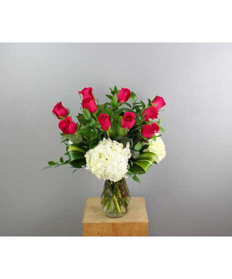 This stunning floral arrangement features a dozen vibrant hot pink roses elegantly arranged in a sleek clear glass vase.