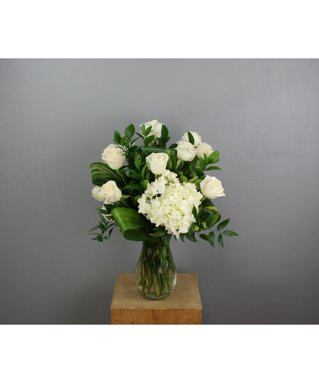 A stunning floral arrangement featuring twelve pristine white roses elegantly arranged in a sleek clear glass vase.